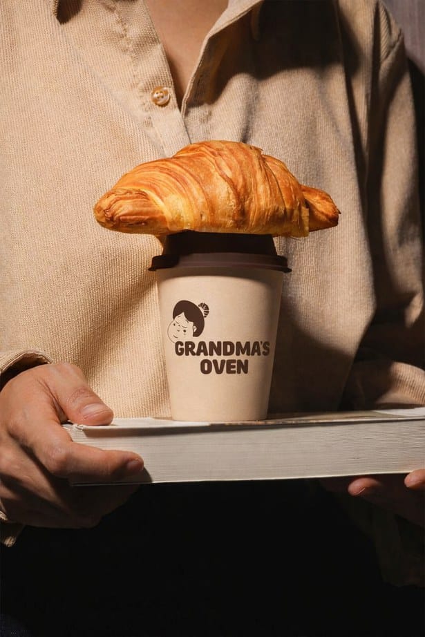 Mockup: a cream coffee cup with the wordmark, a croissant resting on the lid