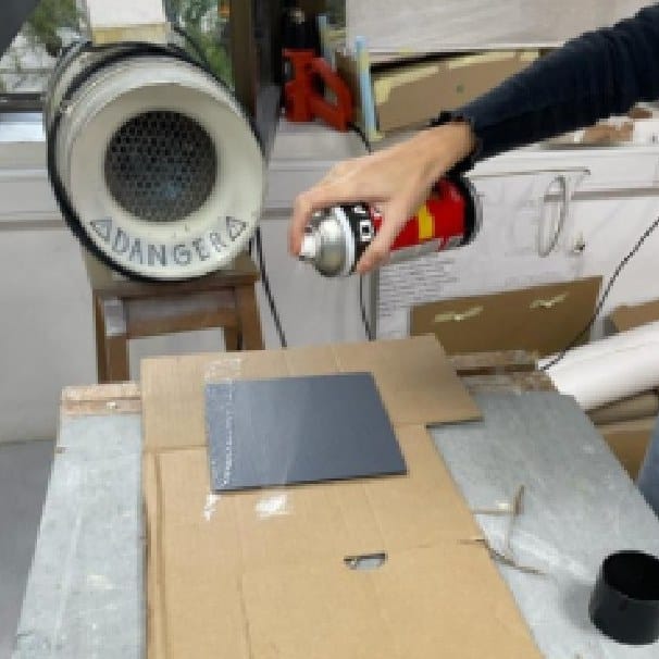 Spray-painting a grey panel in the workshop