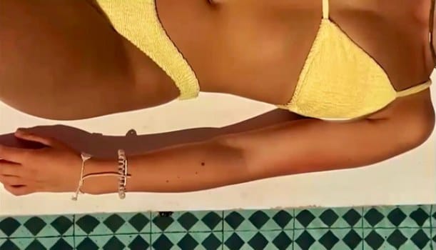 Campaign film still: close-up of a yellow bikini top and arm in the sun