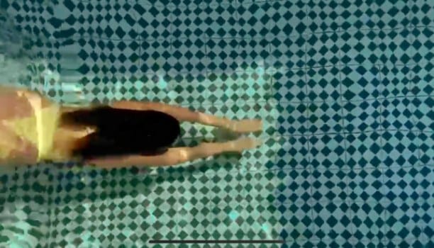 Campaign film still: a swimmer seen from above in a tiled pool