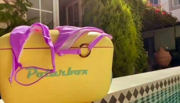 Campaign film still: a yellow cooler box with a lilac bikini draped over it