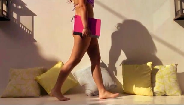Campaign film still: legs walking past yellow cushions, carrying a pink box
