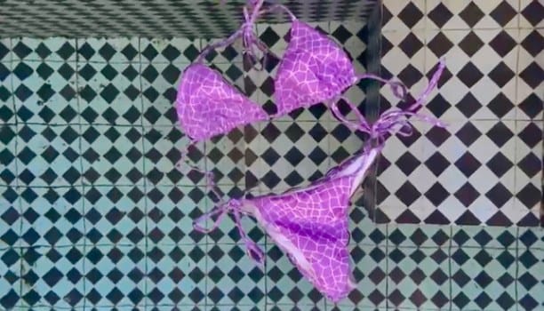 Campaign film still: a purple bikini laid out on black and white tiles