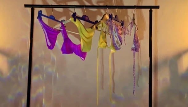 Campaign film still: swimwear hanging on a rail in warm light